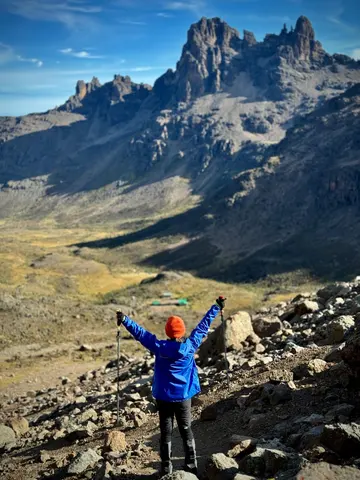 Celebrating tourist looking at peaks during a mount kenya climb with vast plain below